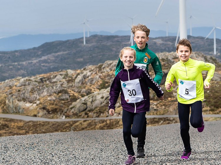a group of children running in the norwegian landscape in a wind energy park